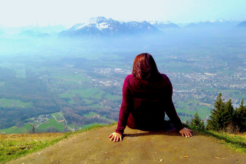 A student sits on a cliff and looks at the mountains.