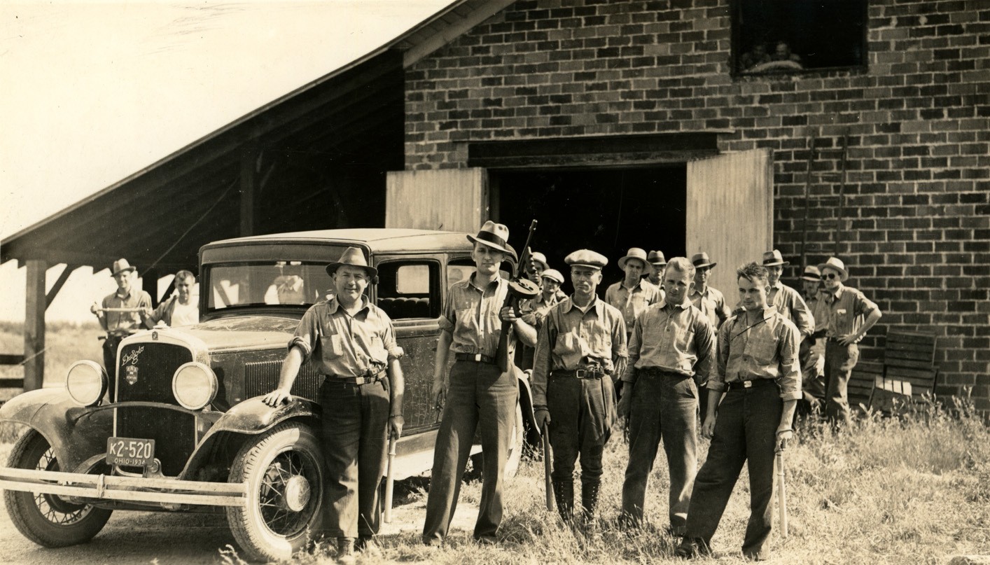 A group of men outside a barn, posing for the camera