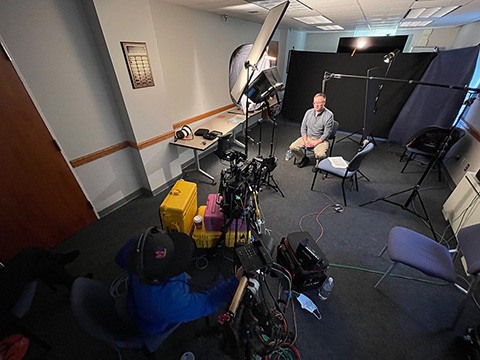 A man sittingin a chair surrounded by studio lighting and equipment.