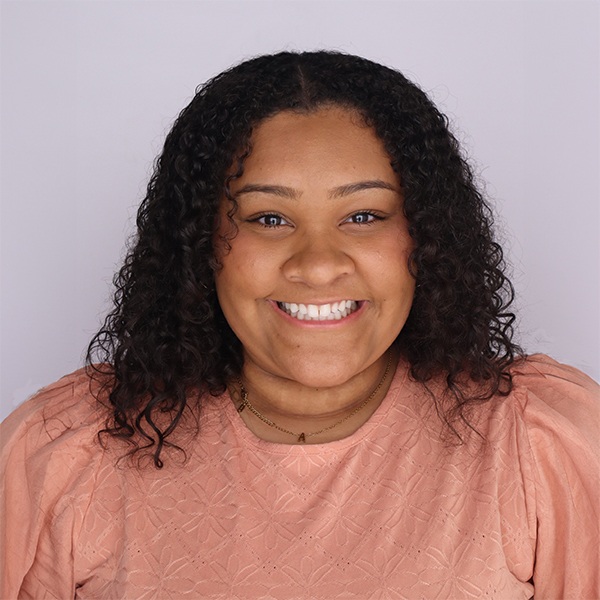 A woman with sholder length curly hair and a peach short sleeve shirt