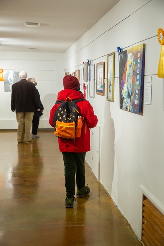 A person in a red coat and hat looking at the paintings