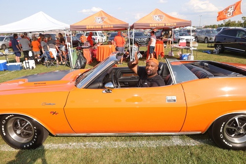 A man waves while driving an orange car