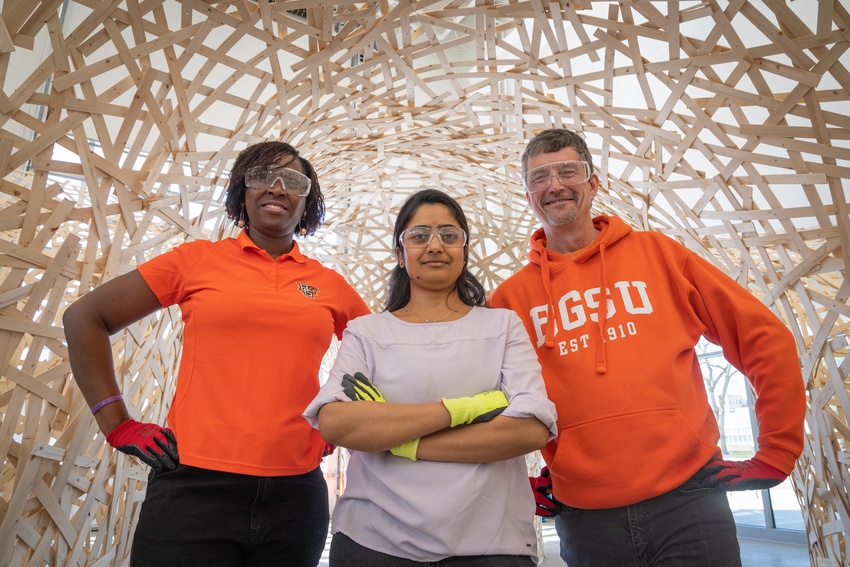 Three people stand in-front of a geometric structure