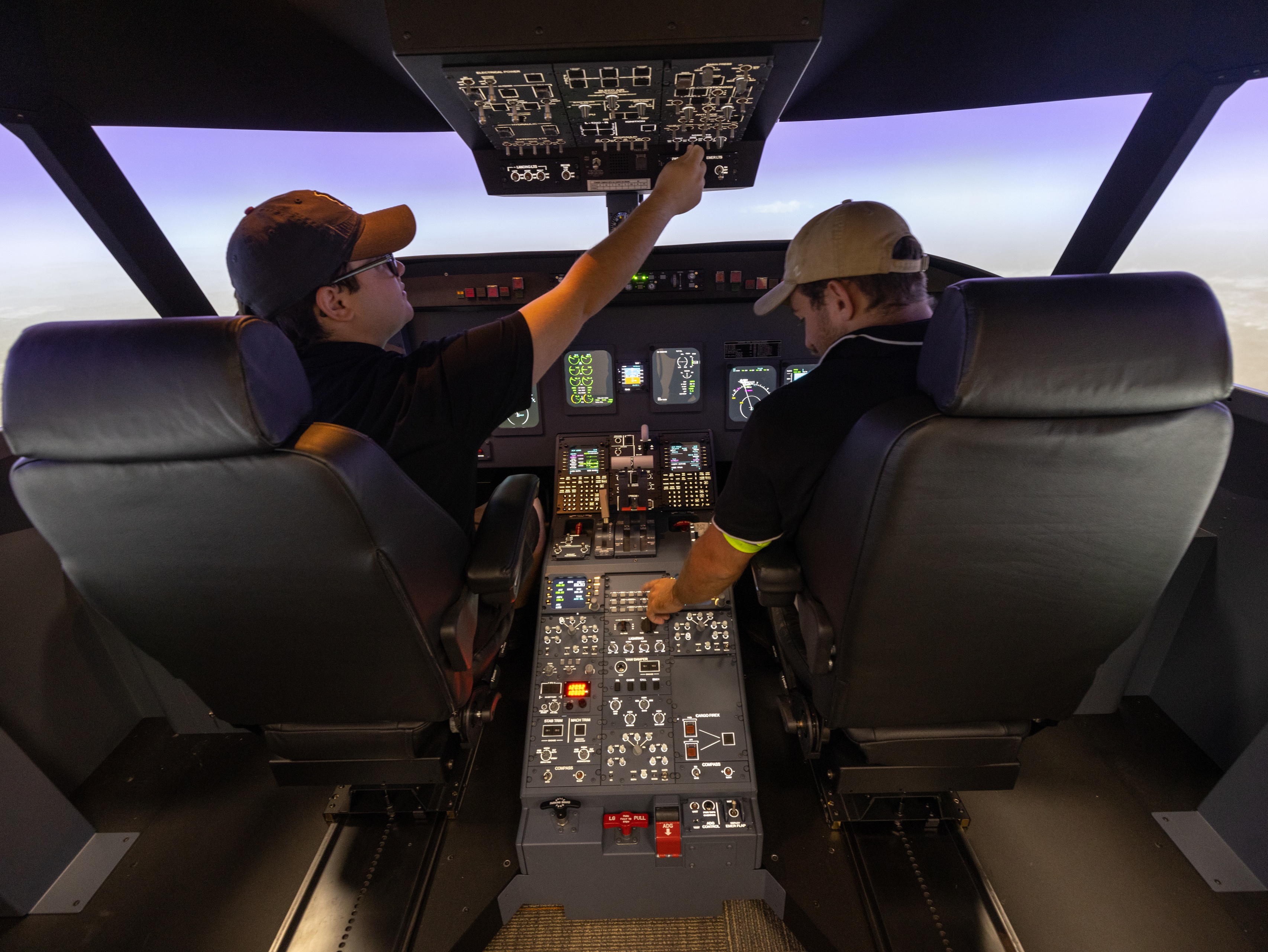 Two aviation students sit inside a flight simulator