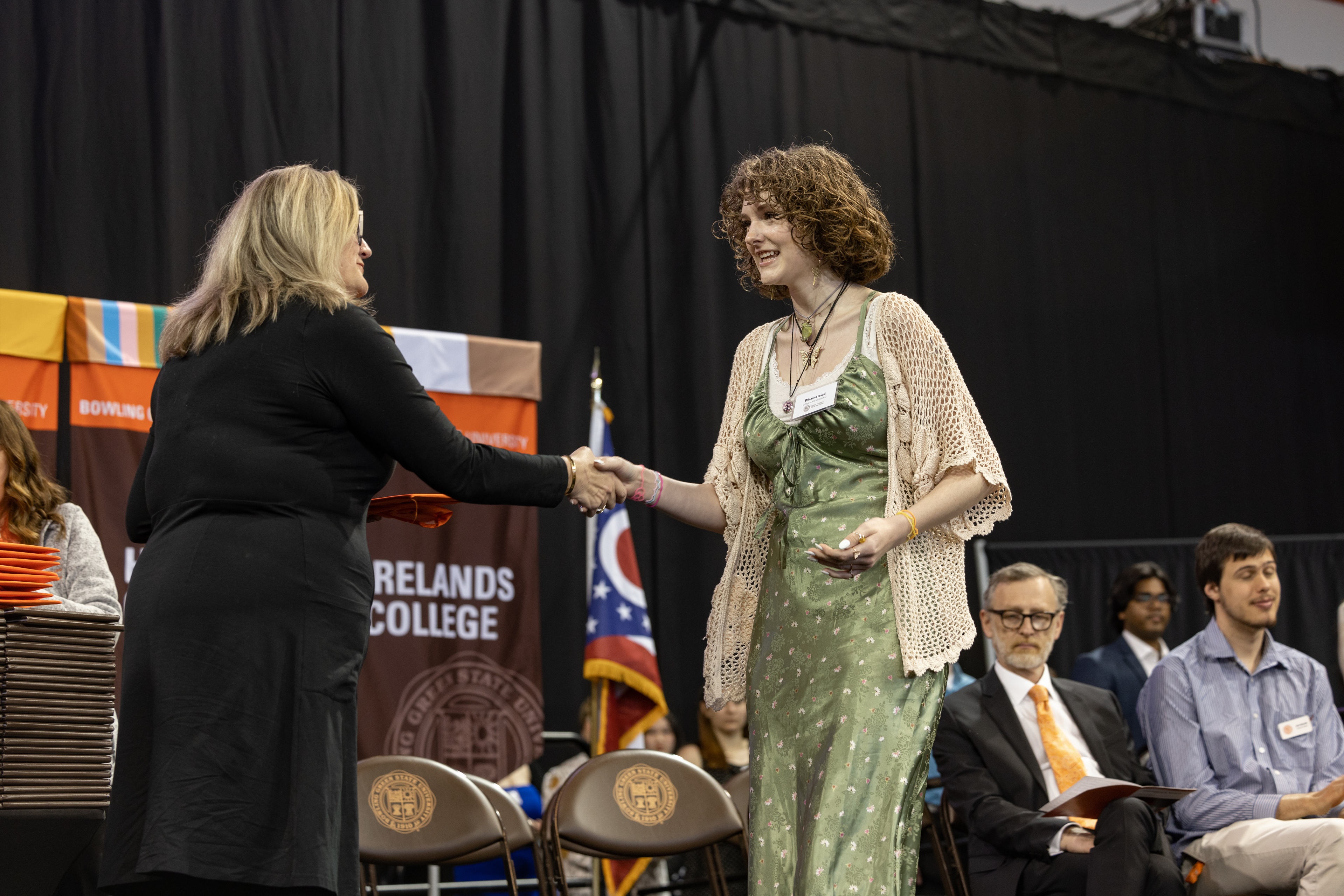 Two women shake hands on a stage.