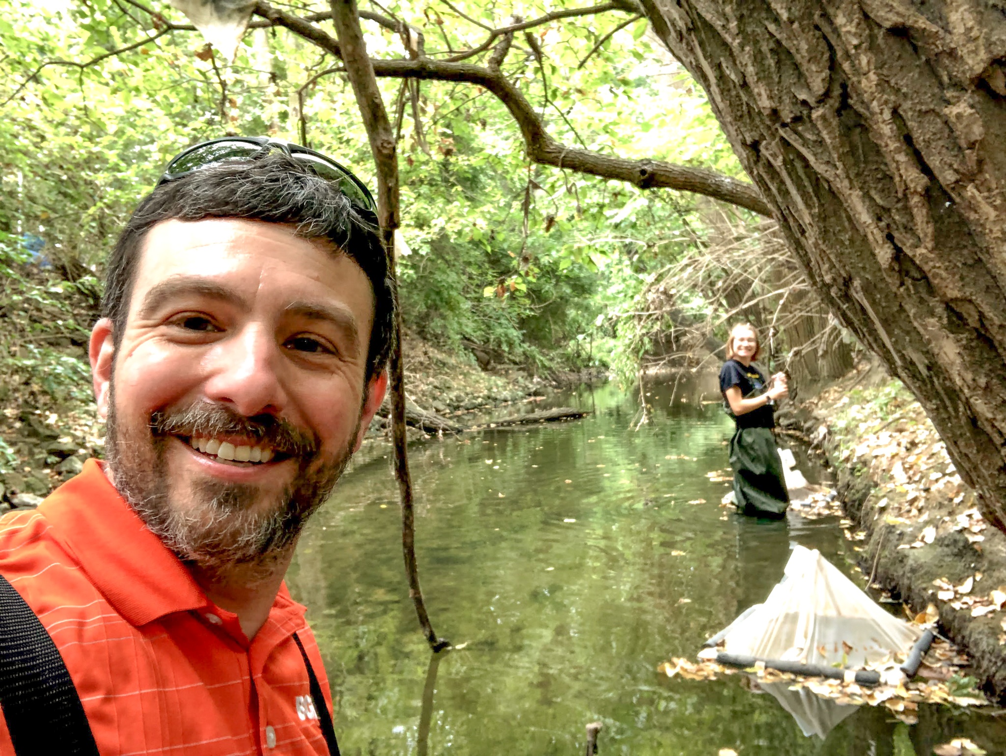 A person takes a selfie while standing in a stream.