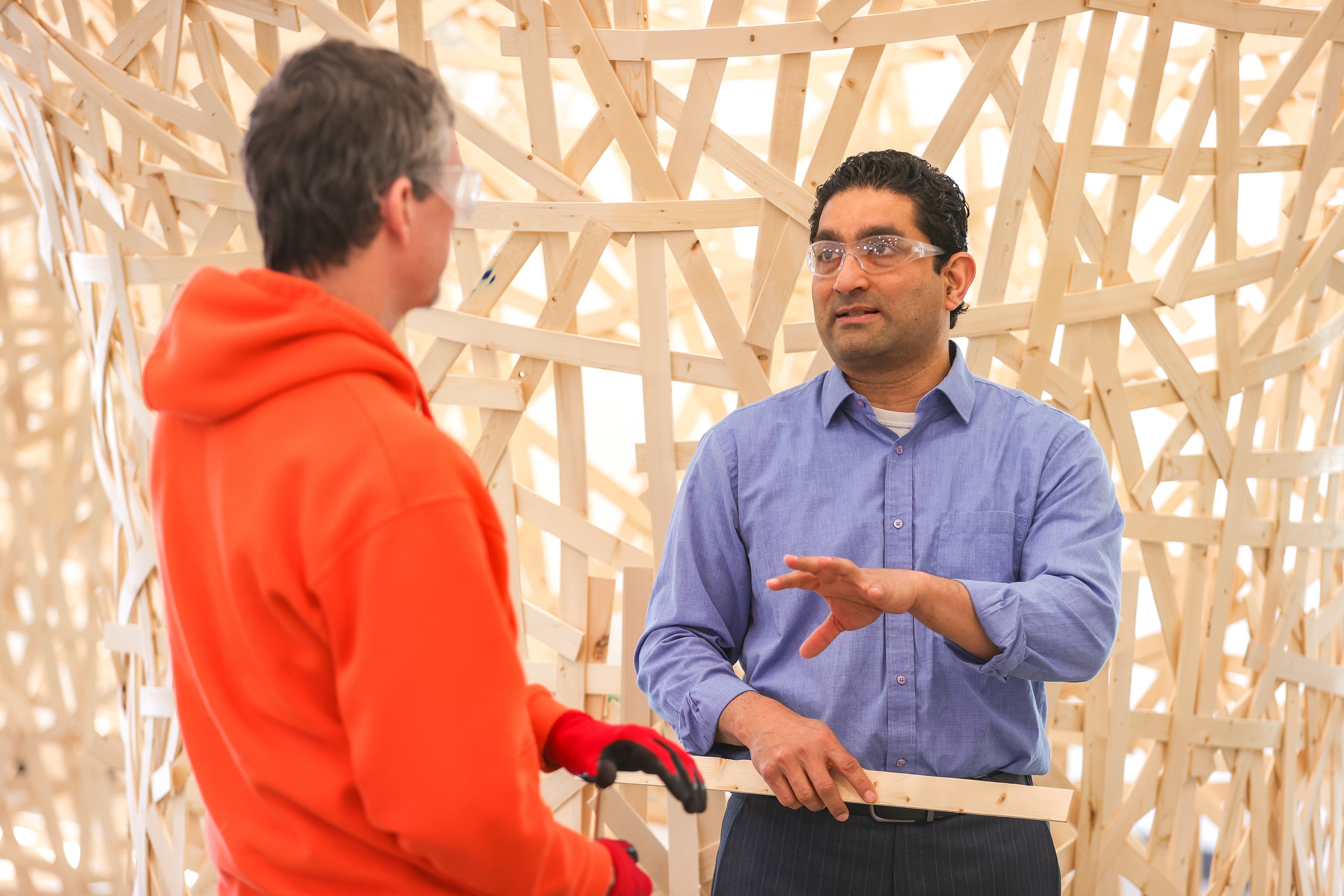 A man gestures near a large wooden structure.