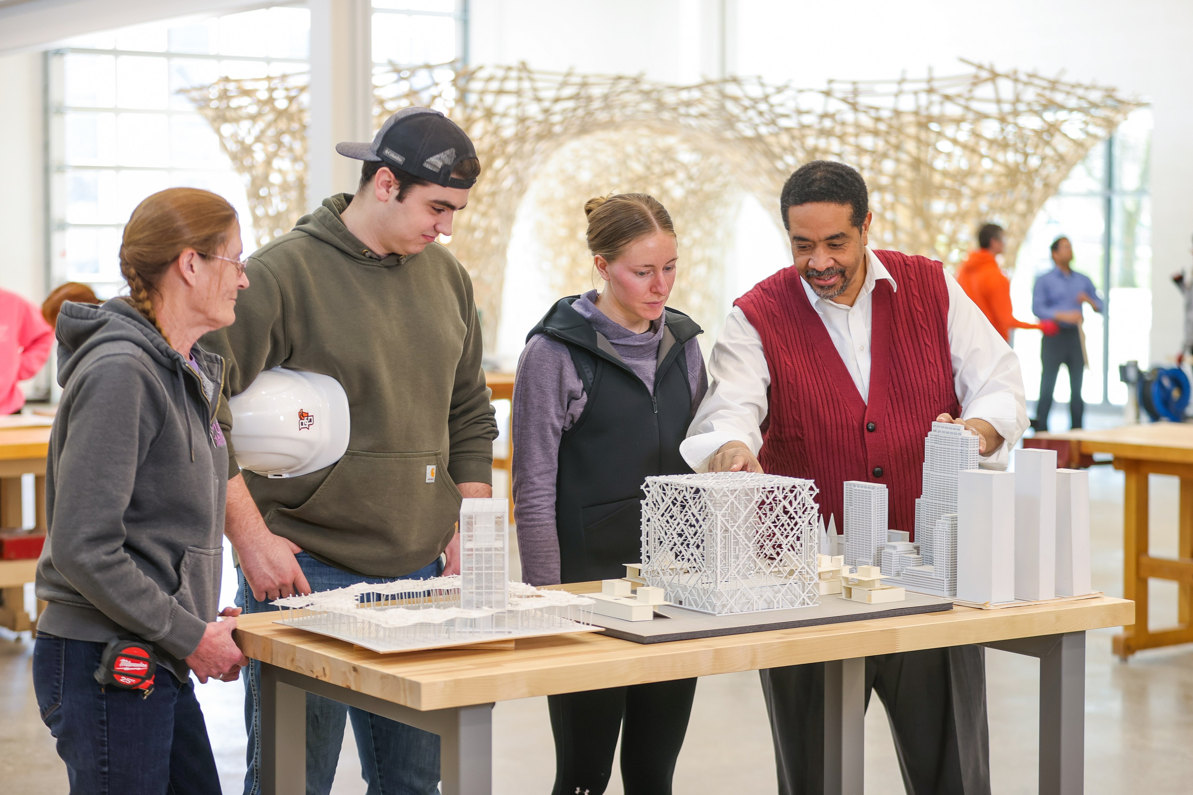 Students and a professor look at a model city on a table.