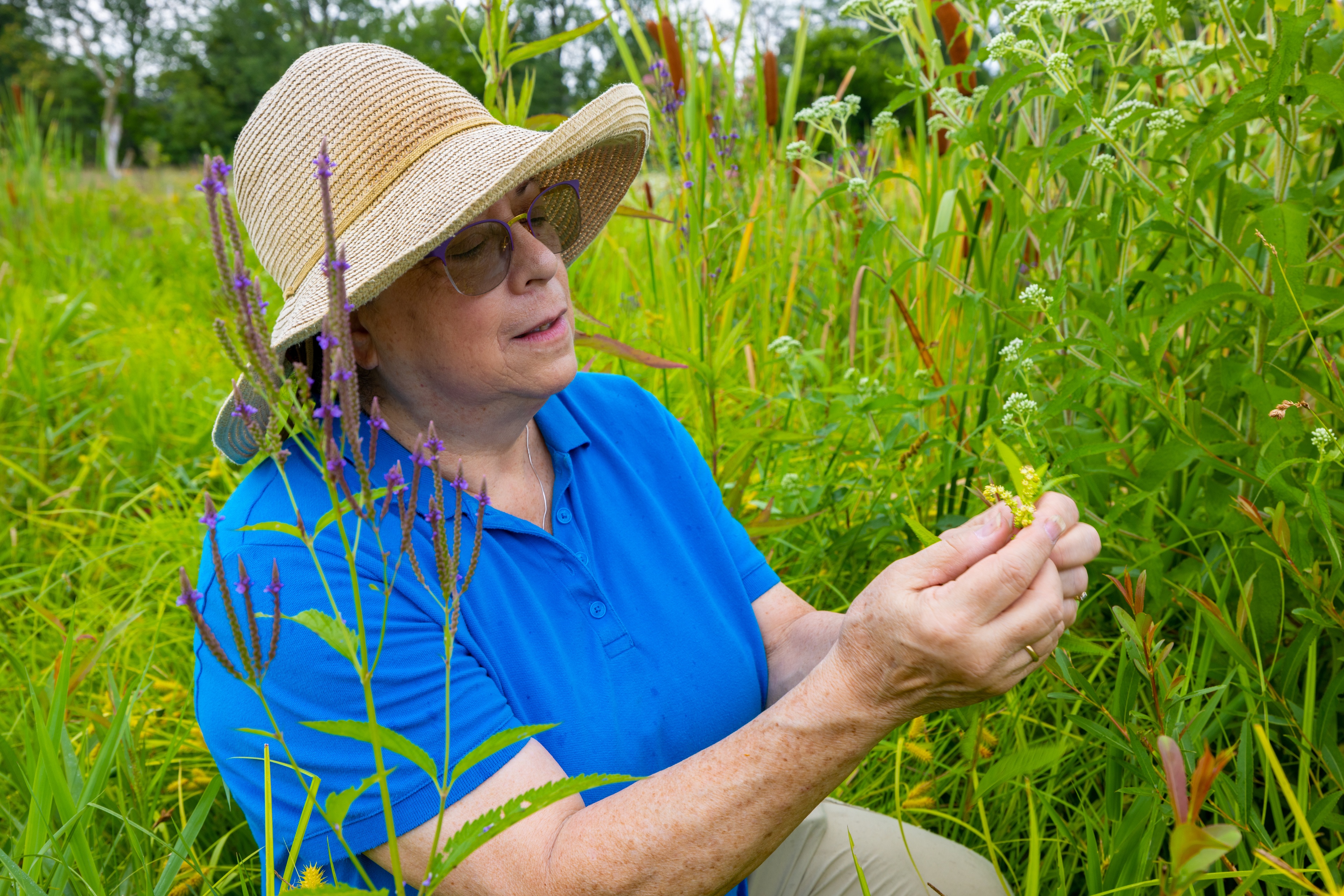 A woman walks through a verdant green area surrounded by plants.