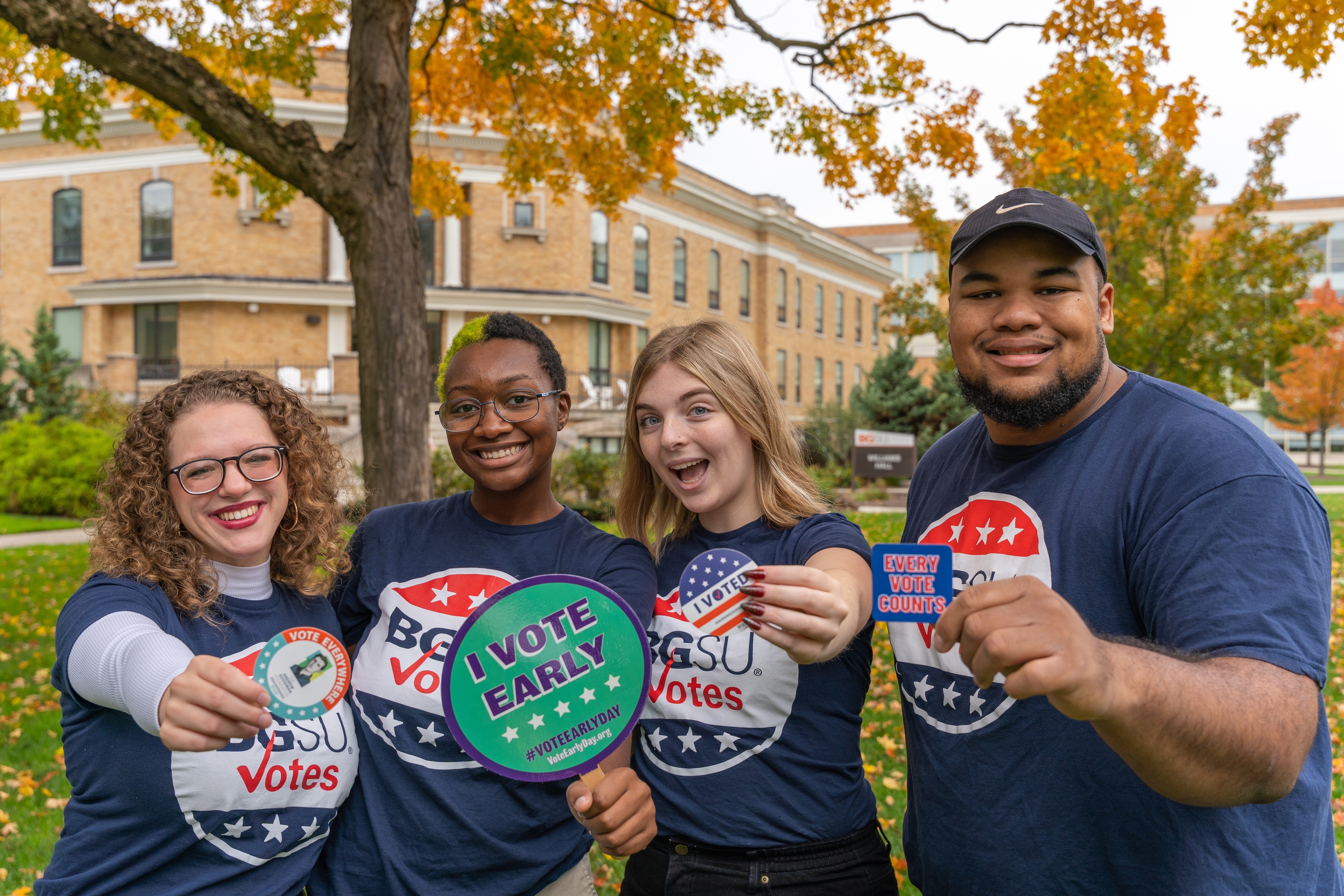 Four BGSU students wearing BGSU Votes shirts hold voting stickers.