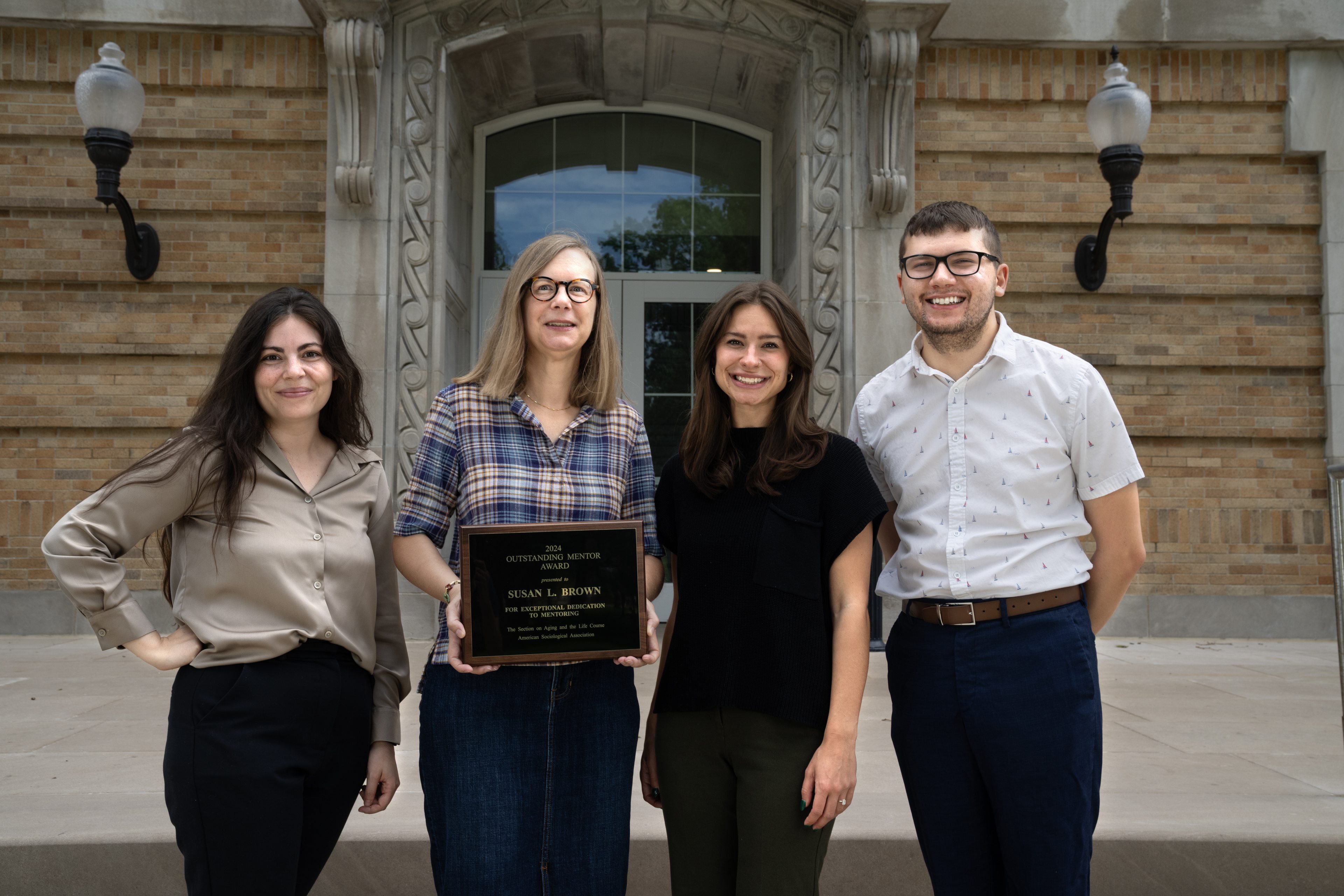 Woman stands in the middle of students holding a plaque