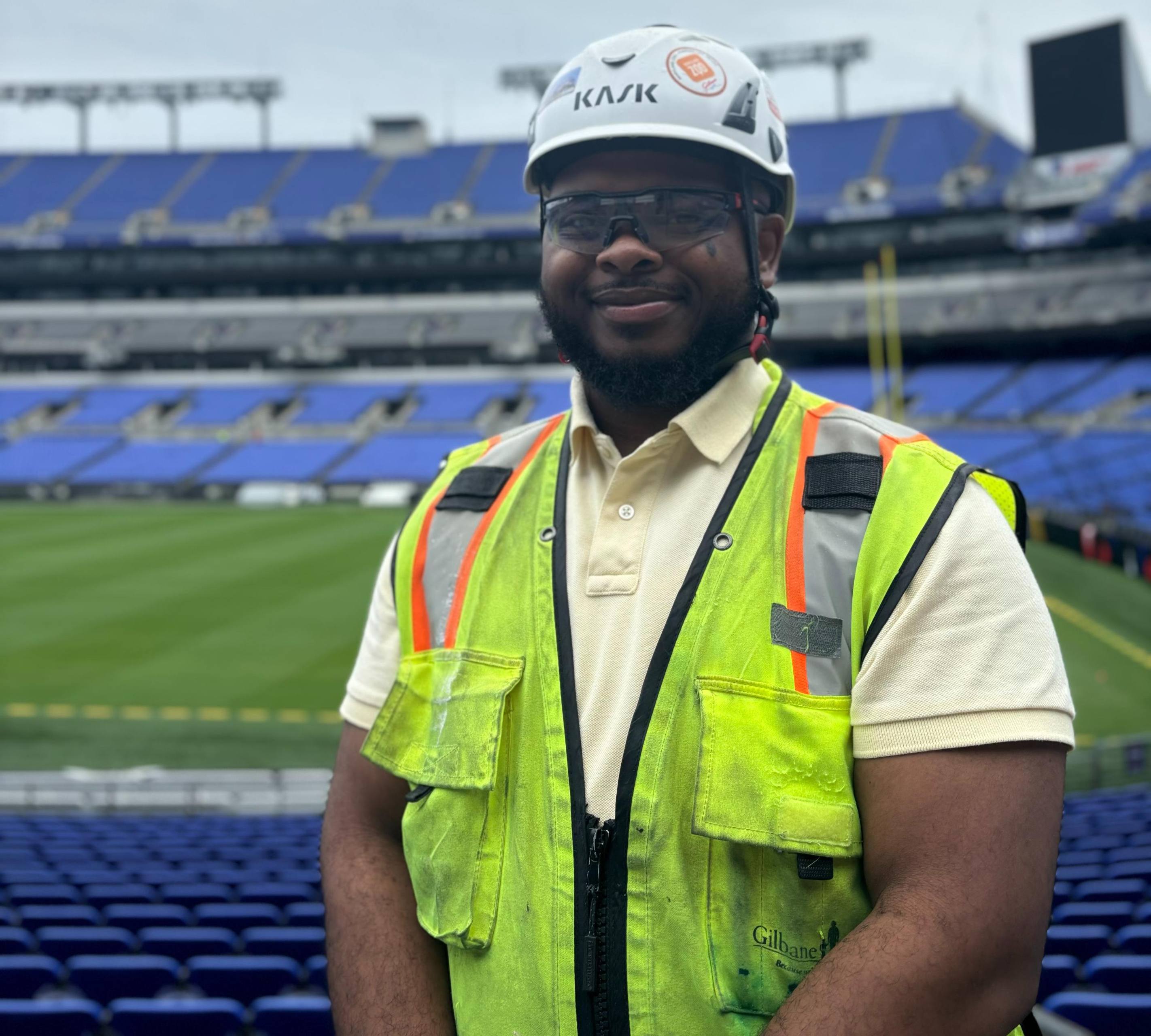 A person wearing a construction hat and vest stands in an empty football stadium.