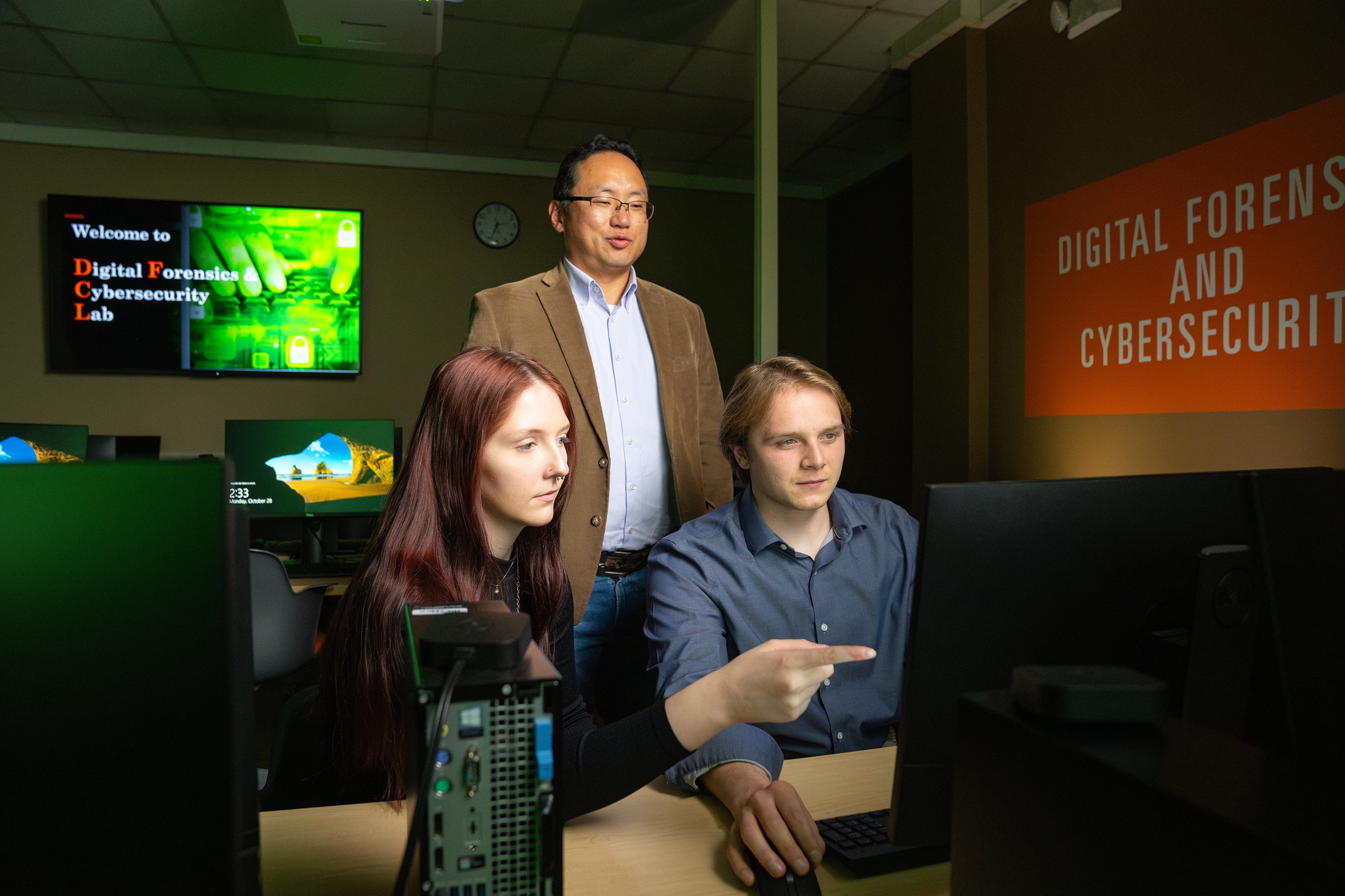 Two students and a professor work on a computer screen