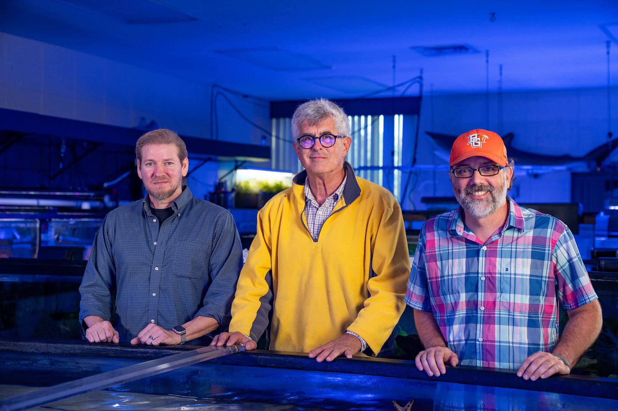 Three professors stand at an aquarium.