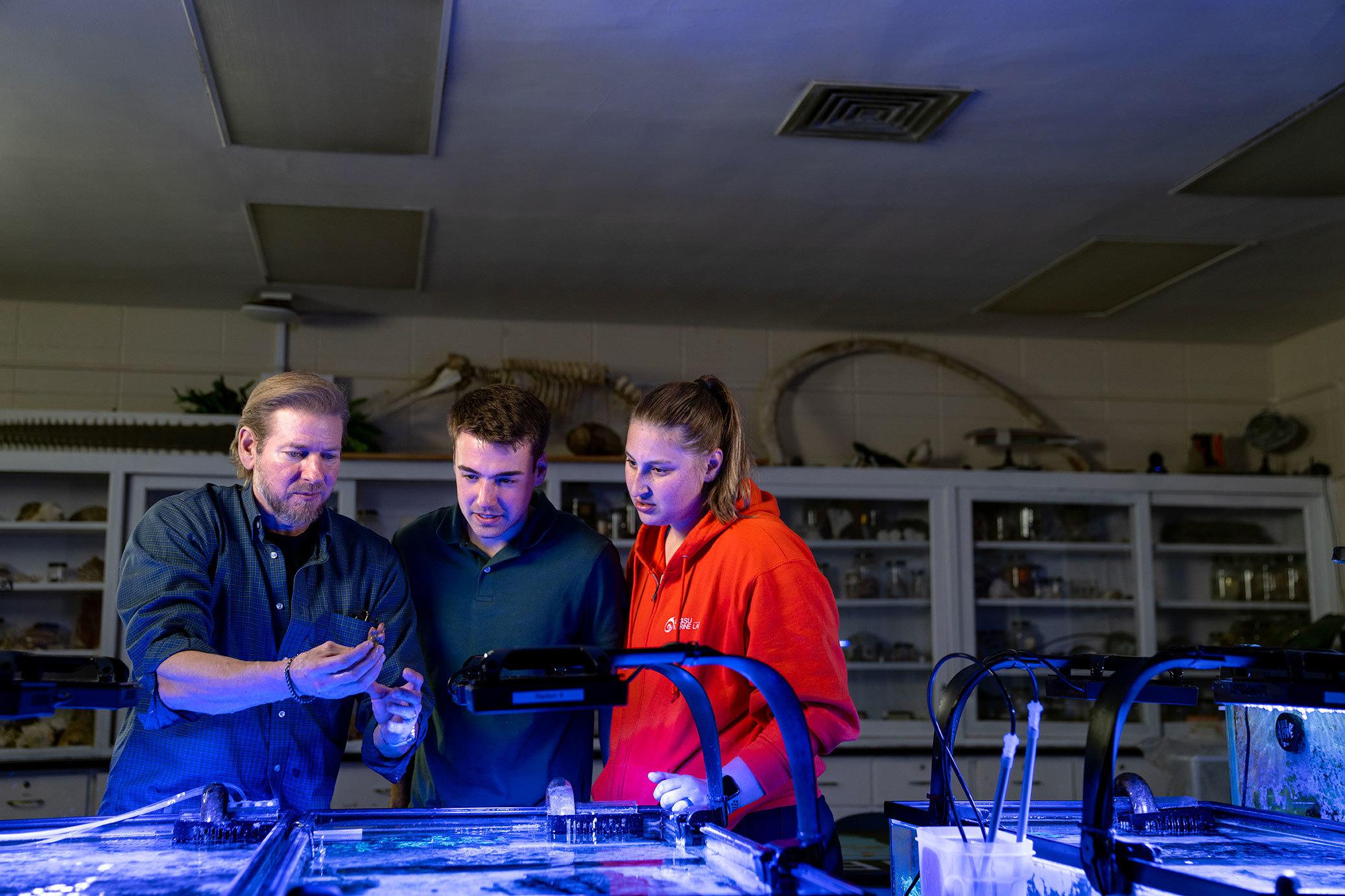 A professor talks to two students near an aquarium.