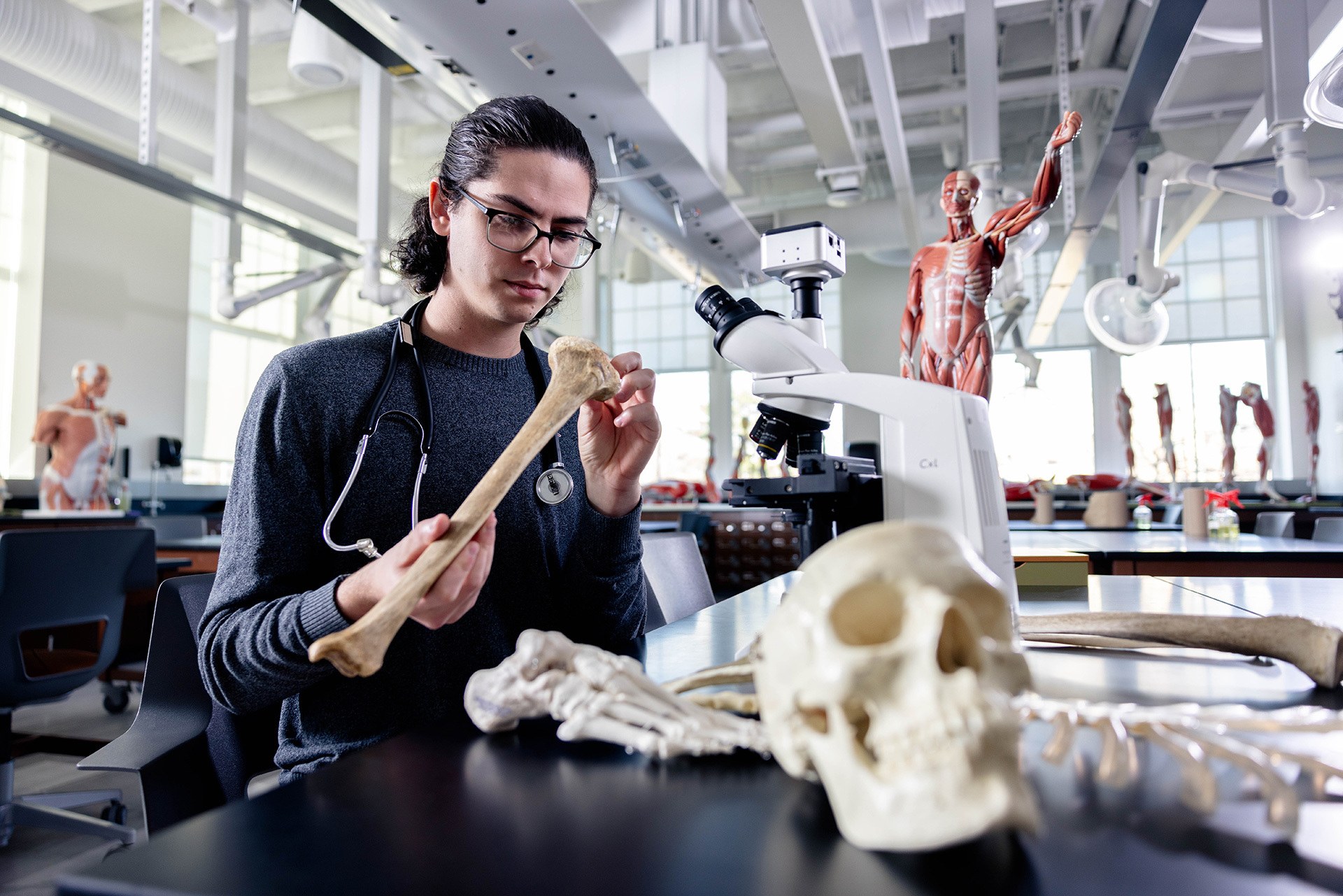 A student holds a bone while wearing a stethoscope in a lab