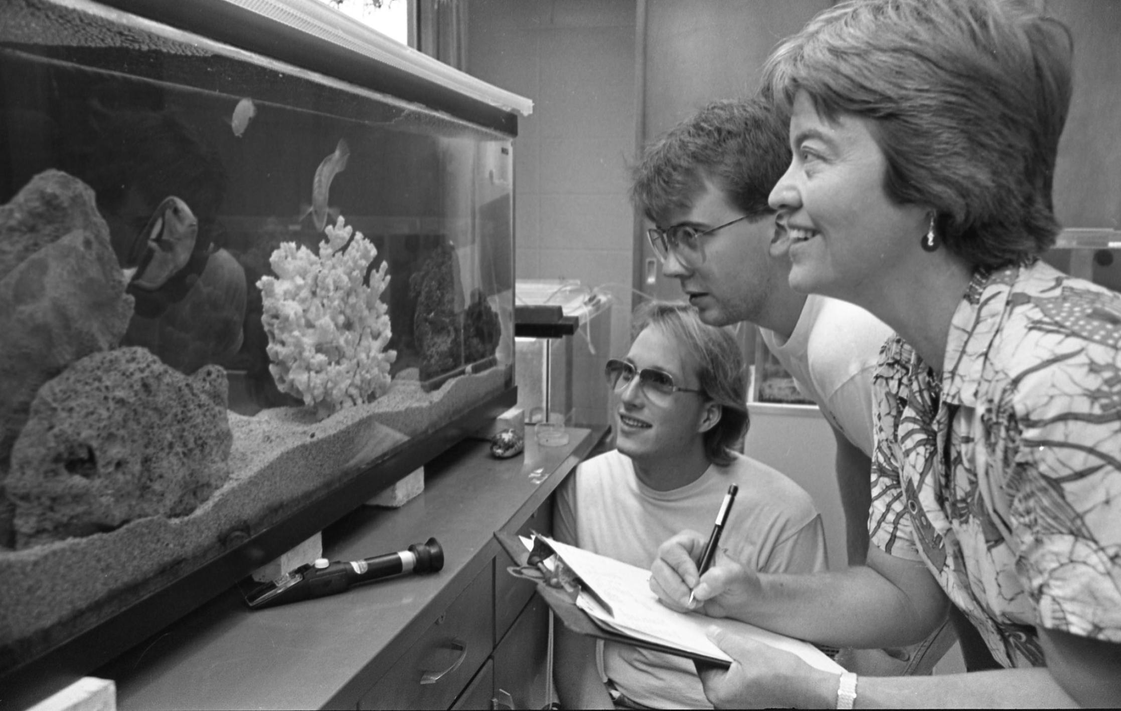 A woman and two students look at a fish tank.