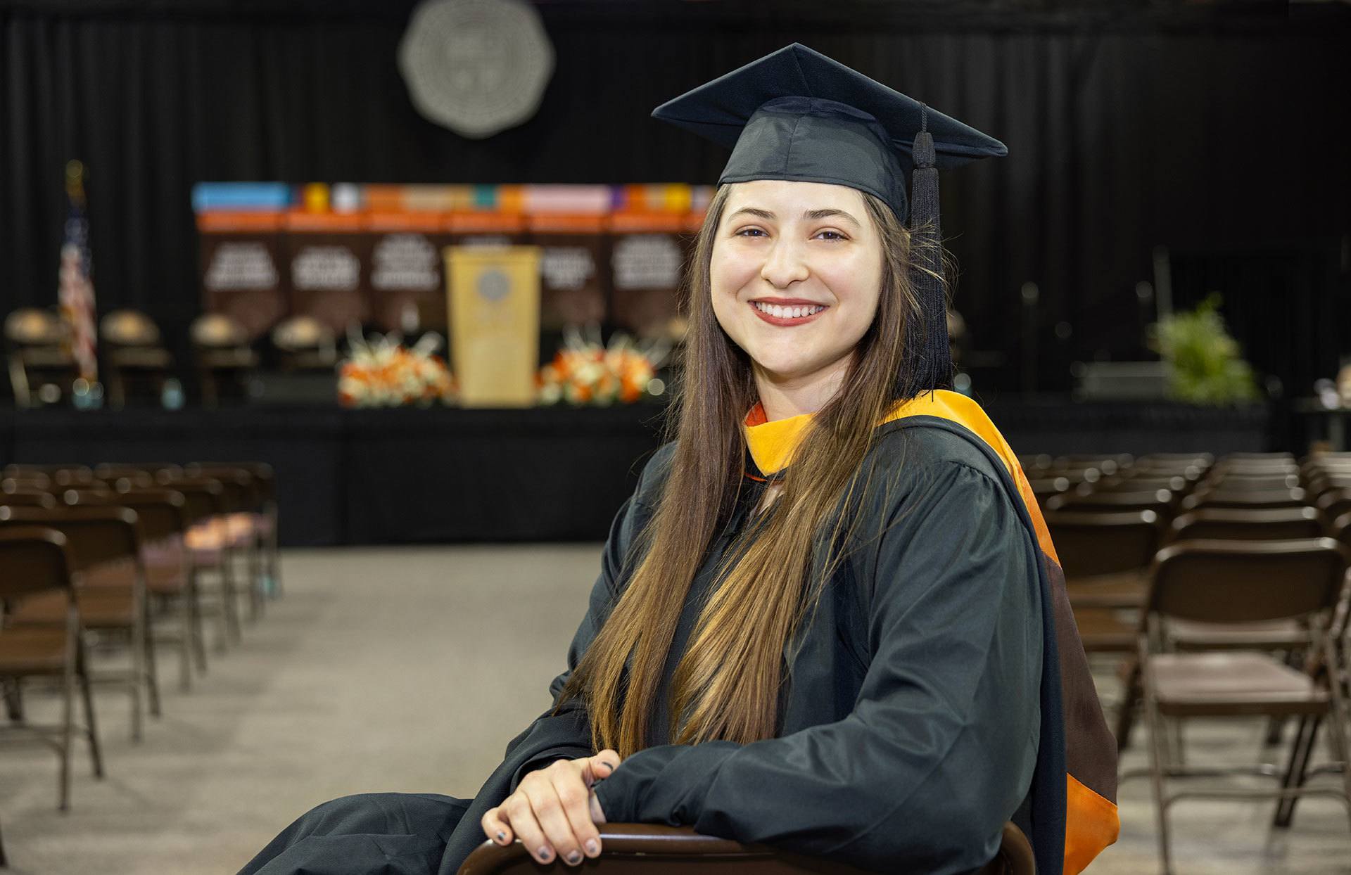 A BGSU graduate sits and smiles in front of the stage.