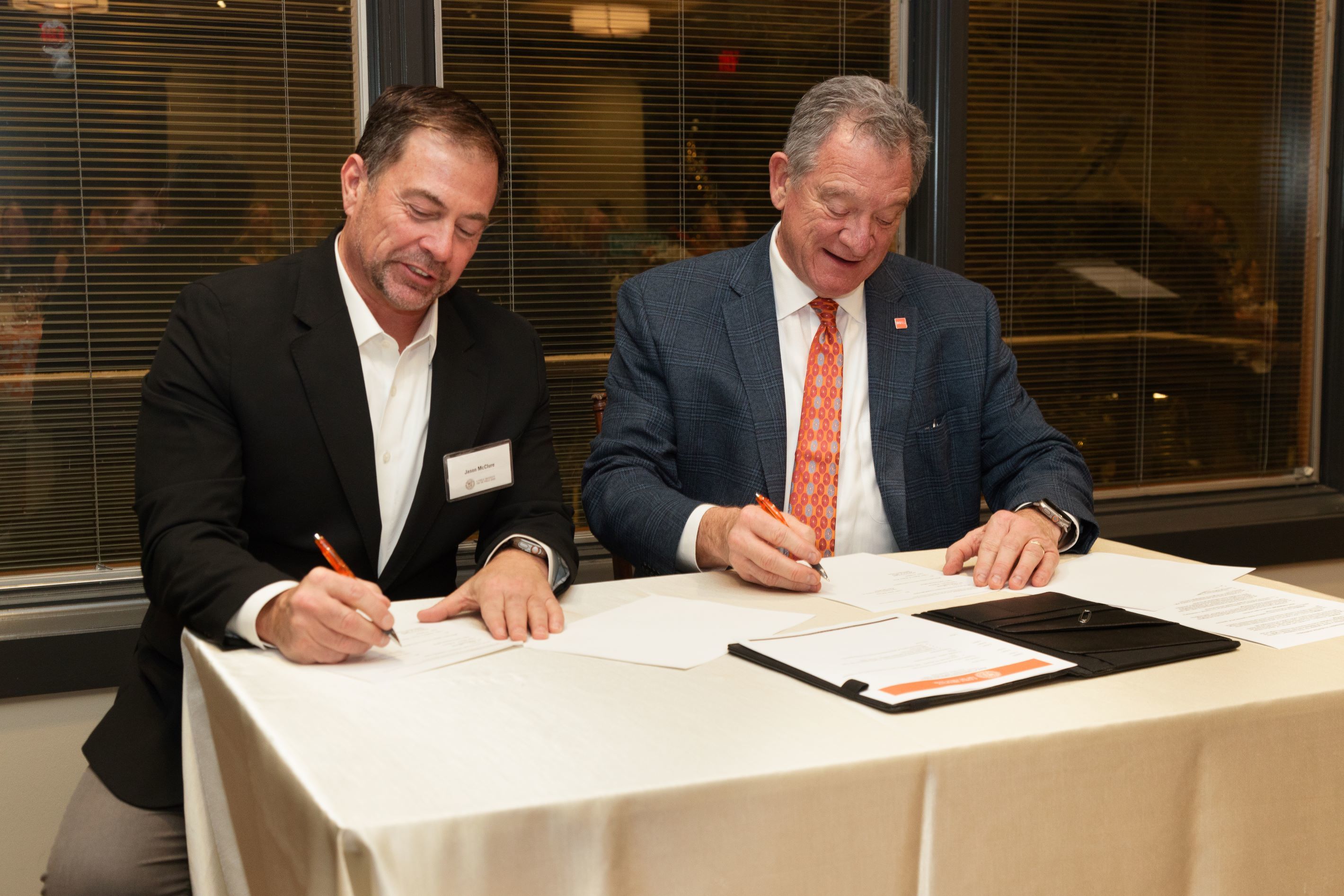 Two people sit at a table and sign papers.