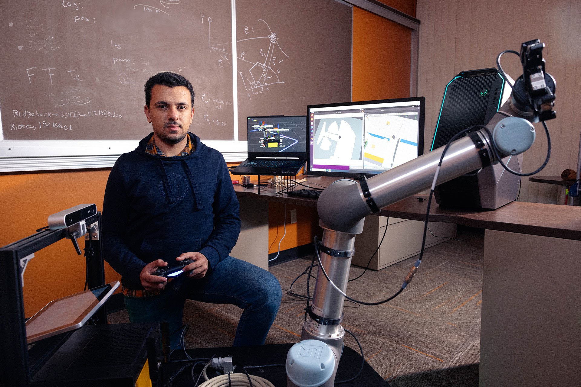 Man sits behind robot with controller in hand