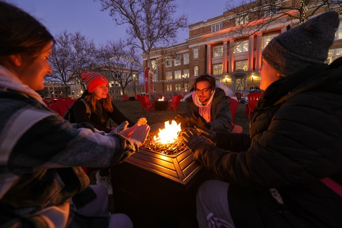 Four students sitting around a fire on campus