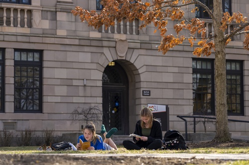 Two individuals lay in the grass while reading books.