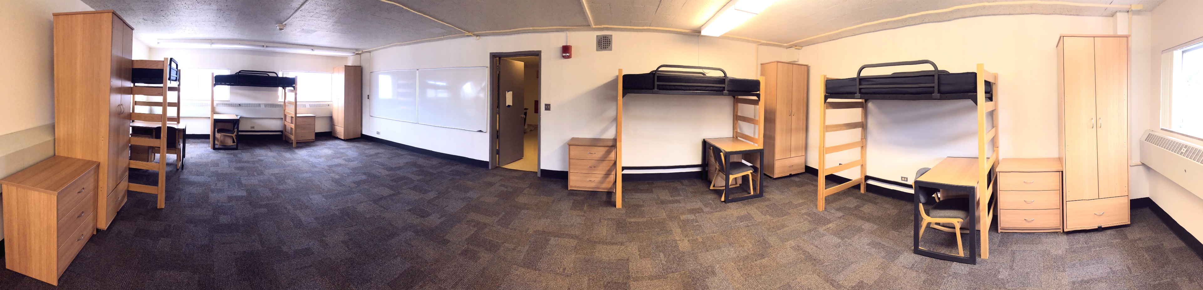 Four beds, dressers, desks and wardrobe panoramic view of the entire room facing the entryway door.