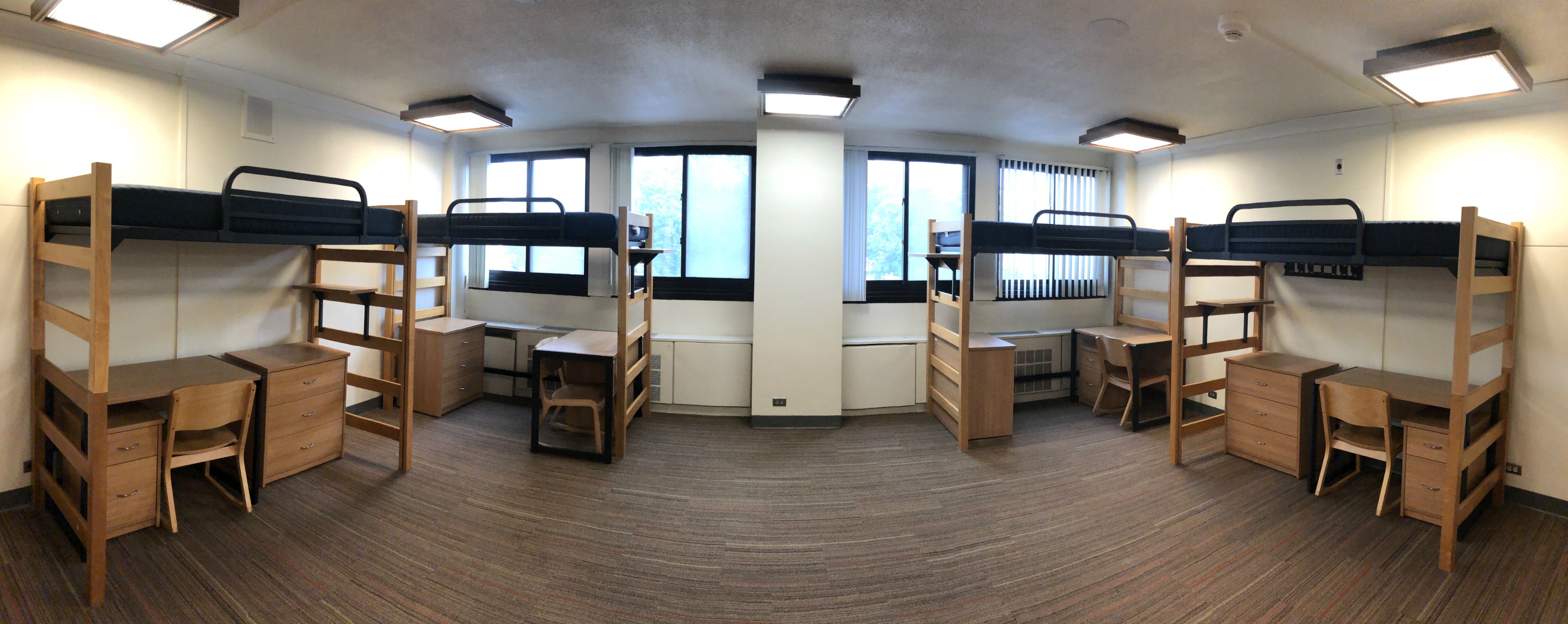 Four beds, dressers, desks and wardrobe panoramic view of the entire room taken from the middle of the room near the entryway door.