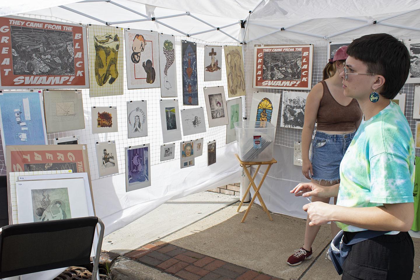 Two people looking at art displayed in tent.