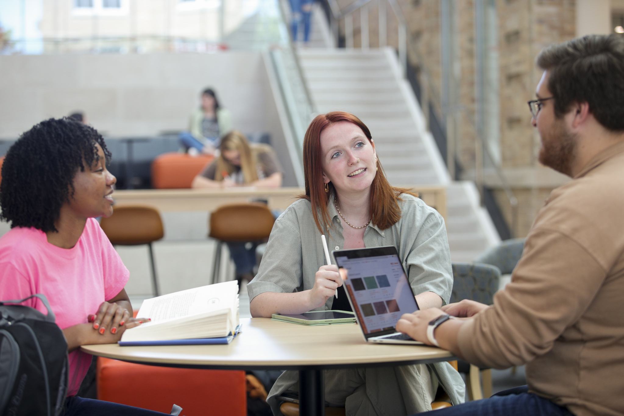 Three students converse around a round table in the atrium of the Maurer Center.